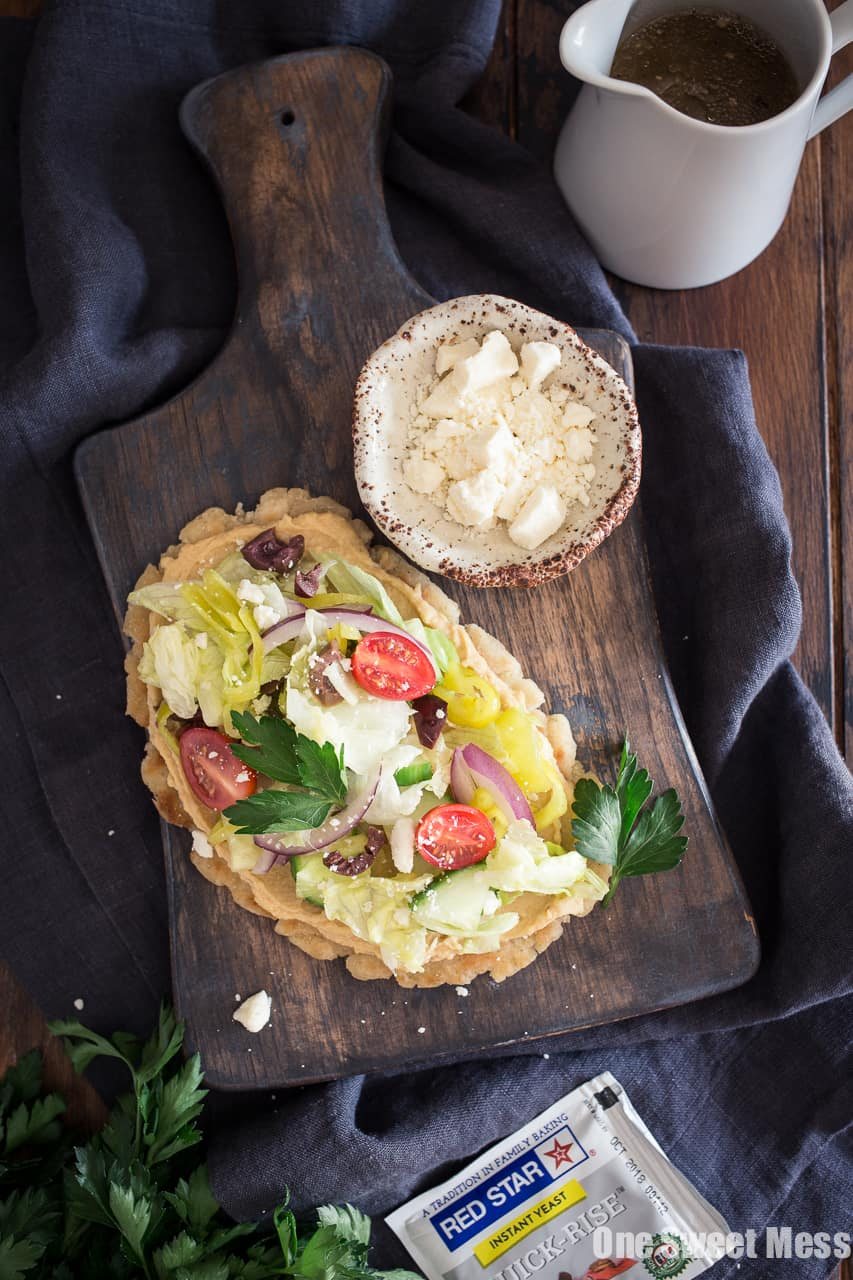 Gluten-Free Greek Salad Naan Pizza: Gluten-Free Naan smeared with creamy hummus and topped with a mound of fresh Greek salad.