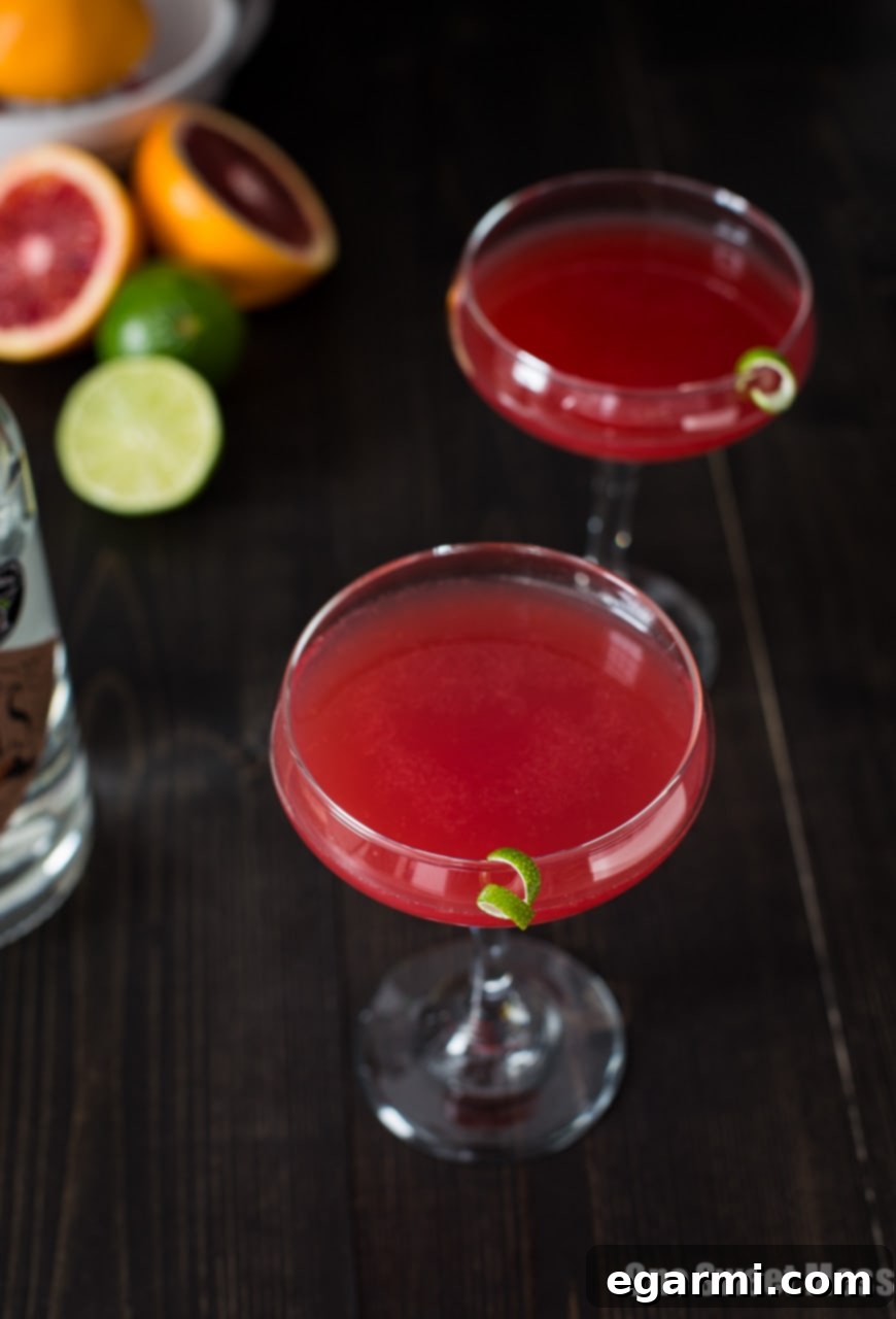 Close-up of a Blood Orange Cosmo cocktail in a glass with condensation, garnished with a fresh blood orange slice.