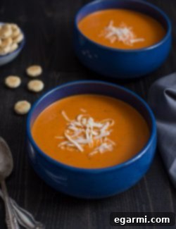 A bowl of creamy Roasted Red Pepper Smoked Gouda Soup with a sprig of fresh herbs.