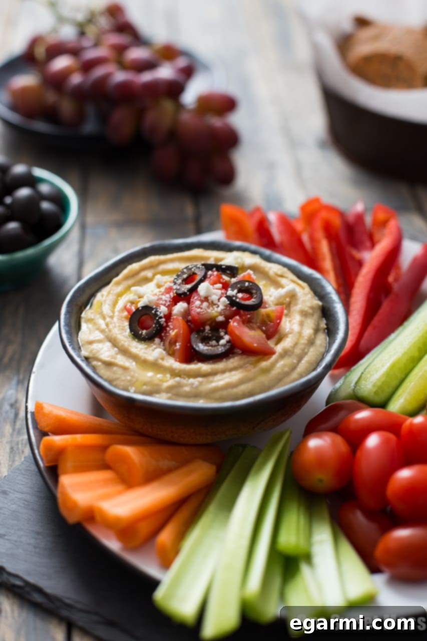 Close-up of a hand dipping fresh cucumber into a Greek Hummus Platter