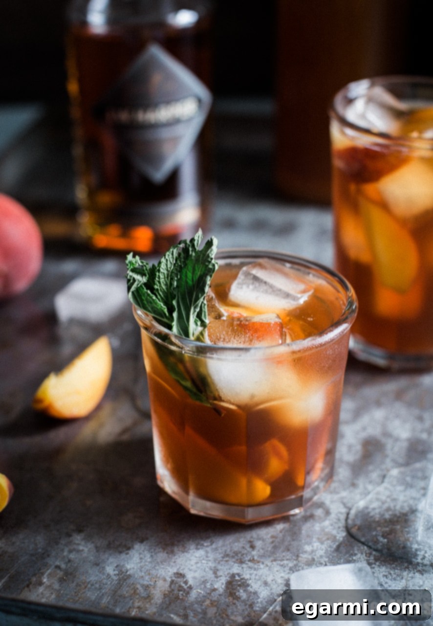 Close-up of a Peach Arnold Palmer with Bourbon cocktail, showing ice cubes, peach slices, and fresh mint