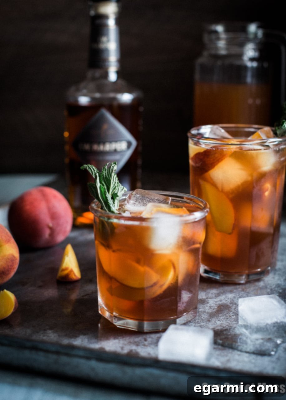 A large pitcher of Peach Arnold Palmer with Bourbon, garnished with fresh peach slices and mint leaves