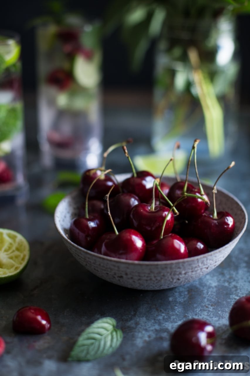 Ingredients for a Black Cherry Mojito including fresh limes, mint leaves, and dark cherries on a wooden table