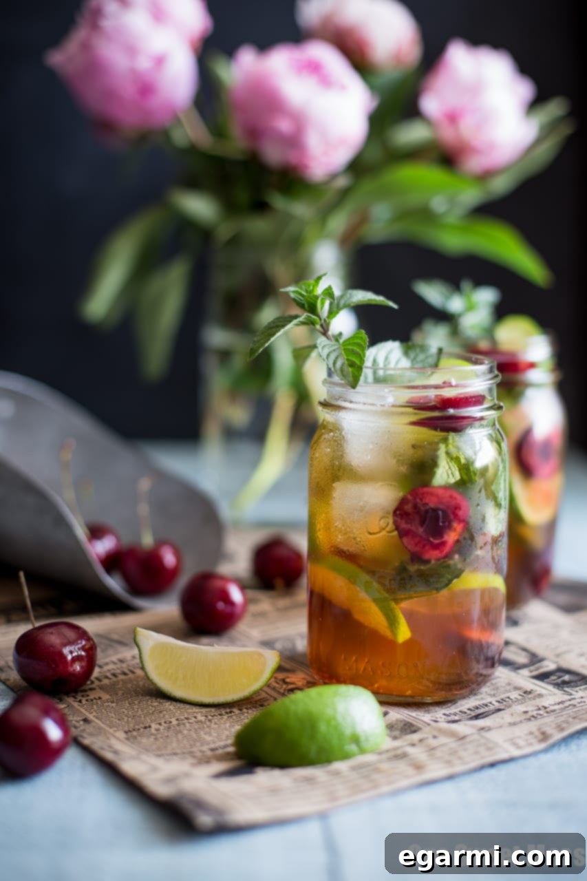 Close-up of a Black Cherry Mule cocktail in a mason jar, showcasing the vibrant red color and fresh garnishes