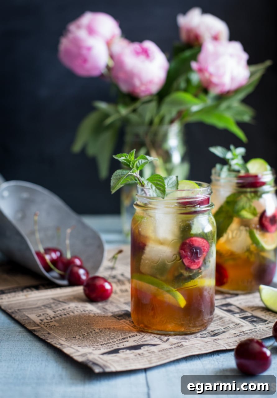 Ingredients for a Black Cherry Mule laid out on a table: cherries, lime, mint, whiskey, and ginger beer
