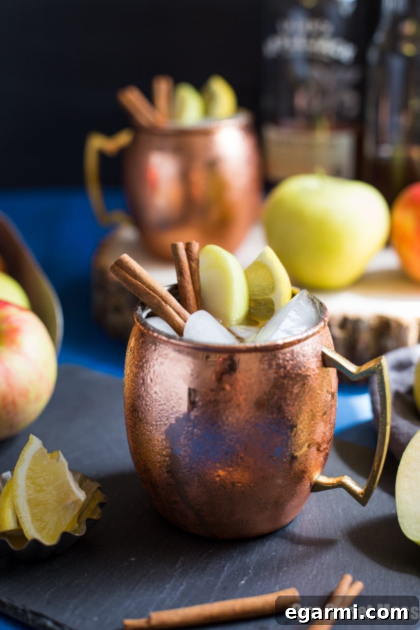 Close-up of an Apple Pie Mule, highlighting the ice, apple slices, and cinnamon stick garnish.
