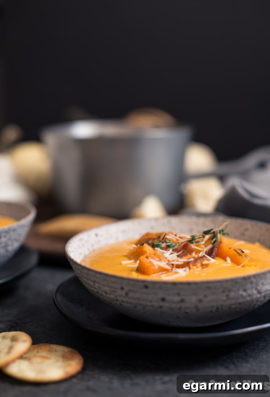 Close-up of a vibrant orange Roasted Butternut Squash & Sweet Potato Soup, served in a rustic bowl.