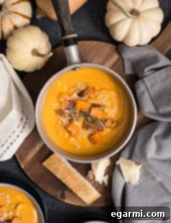 A beautifully garnished bowl of Roasted Butternut Squash & Sweet Potato Soup alongside fresh ingredients.