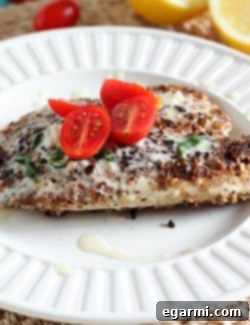 A single serving of Hazelnut Crusted Tilapia with Lemon Butter Sauce on a white plate, garnished with basil and lemon slices