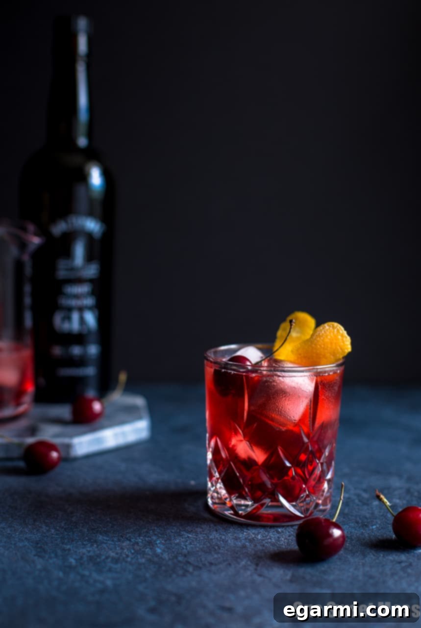 Close-up of a finished Cherry Negroni Cocktail with orange peel and fresh cherry garnish.