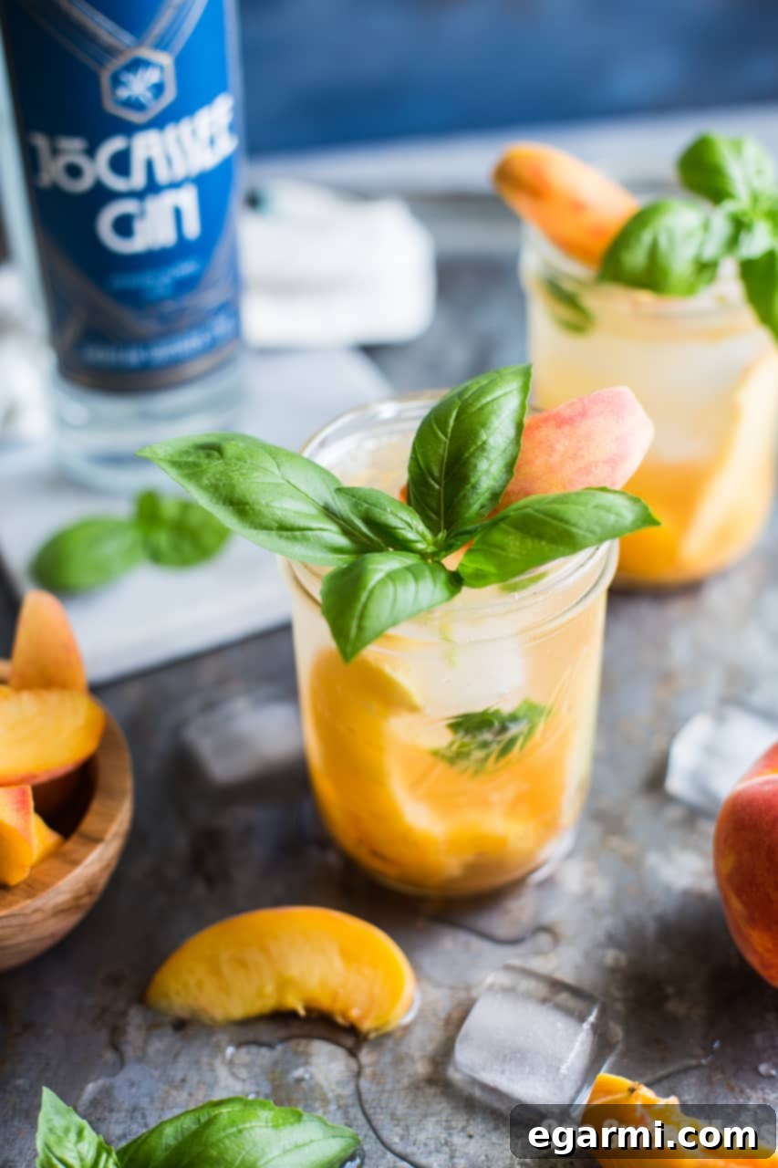 Close-up of a refreshing Peach Basil Gin Fizz cocktail, showing muddled peaches and basil leaves