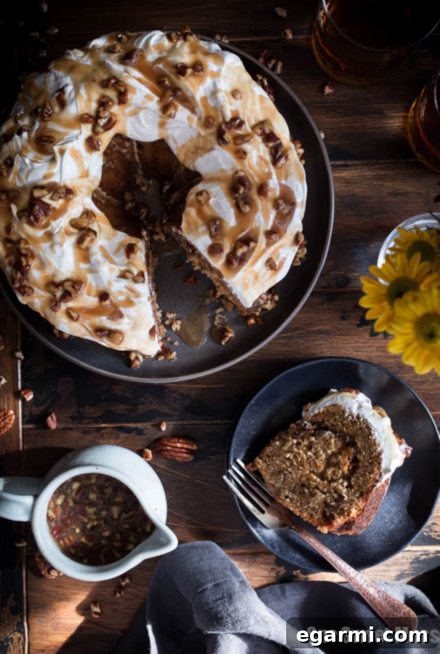 Fully decorated Sweet Potato Bundt Cake with Marshmallow Frosting and Bourbon Pecan Caramel Drizzle on a pedestal