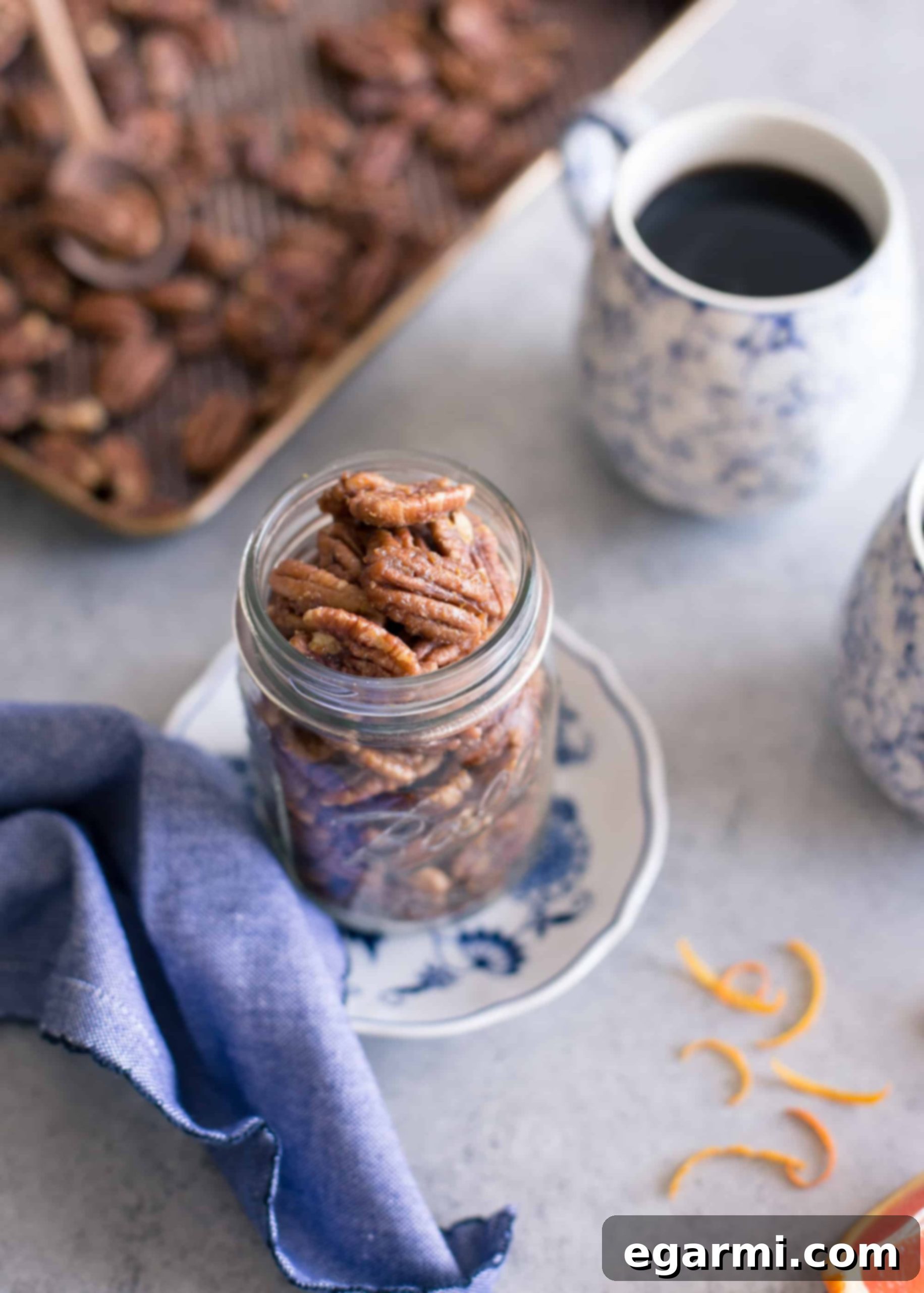 A clear glass jar filled with Maple-Orange Roasted Pecans sits on a wooden table, emphasizing easy access.