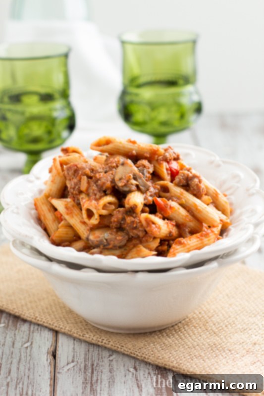 Plated penne pasta with Sausage & Mushroom Ragu, garnished with fresh herbs.