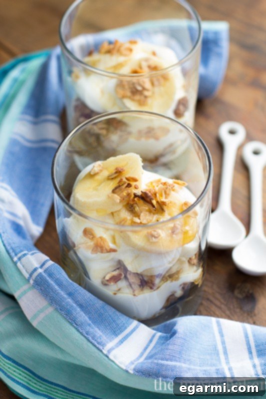Top-down view of a freshly assembled Banana Bread Parfait in a glass, showcasing the creamy yogurt, crunchy granola, and ripe banana layers