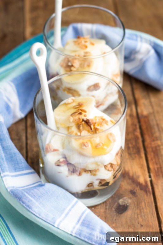 A vibrant Banana Bread Parfait in a clear glass, showing off its distinct layers of creamy Greek yogurt, golden banana maple granola, and fresh banana slices