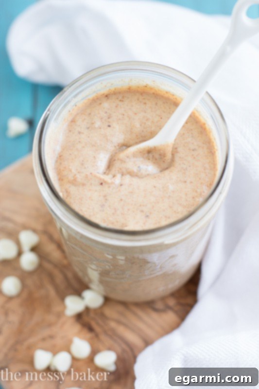 A spoon scooping creamy white chocolate cinnamon almond butter from a jar