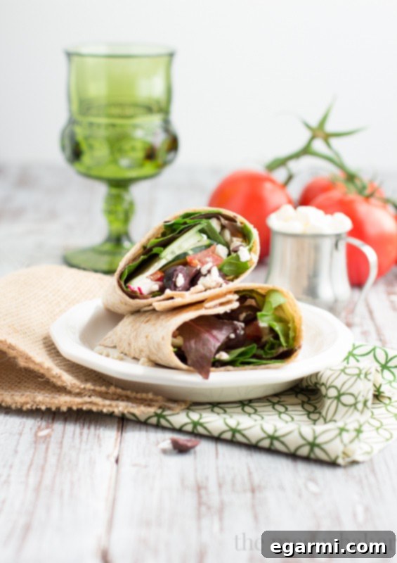 Hands preparing a Greek Salad Wrap, demonstrating the rolling process