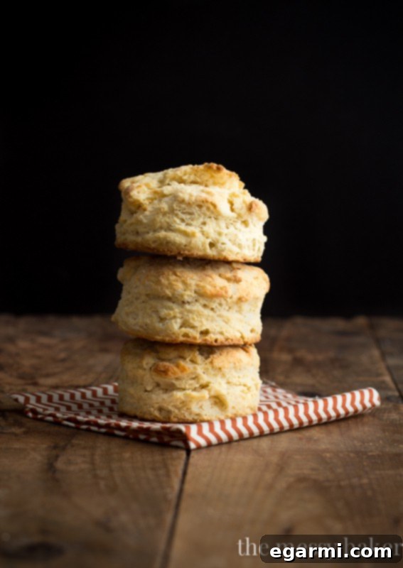 Three golden brown, tall buttermilk biscuits stacked on a white plate, ready to be served.