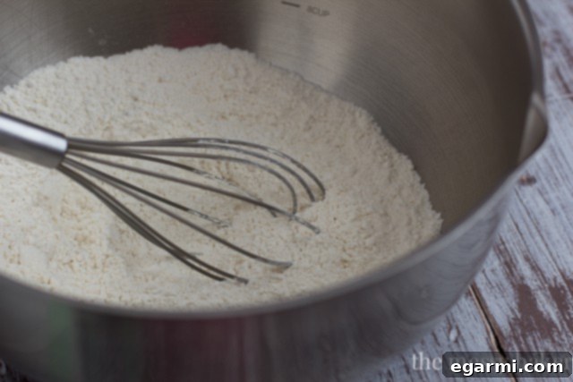 Dry ingredients for buttermilk biscuits, including flour and baking powder, being whisked in a large metal bowl.