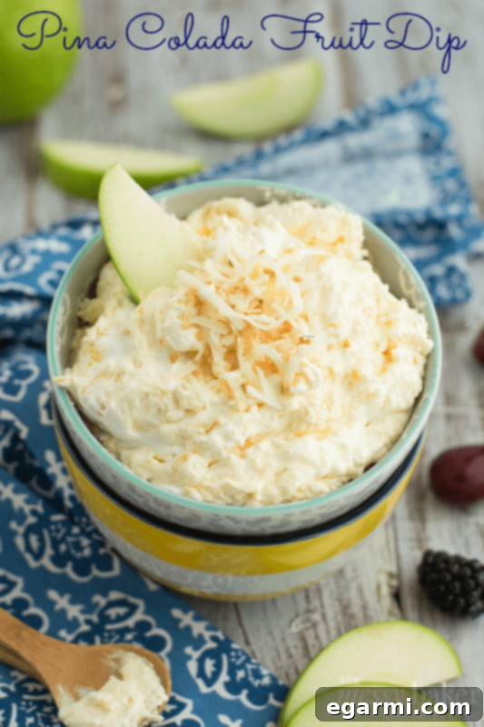 Close-up of creamy Pina Colada Fruit Dip in a glass bowl, garnished with toasted coconut, surrounded by fresh pineapple and berries.