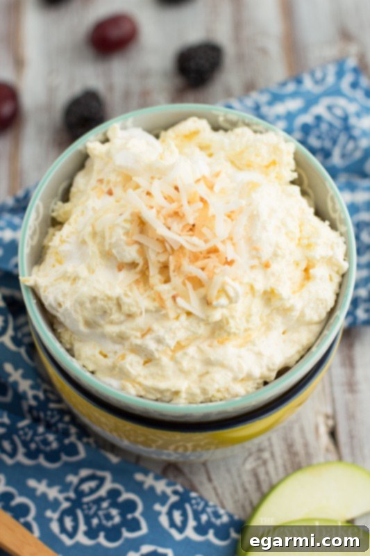 Pina Colada Fruit Dip in a bowl with a spoon, ready for dipping fresh fruit like strawberries, grapes, and apple slices.