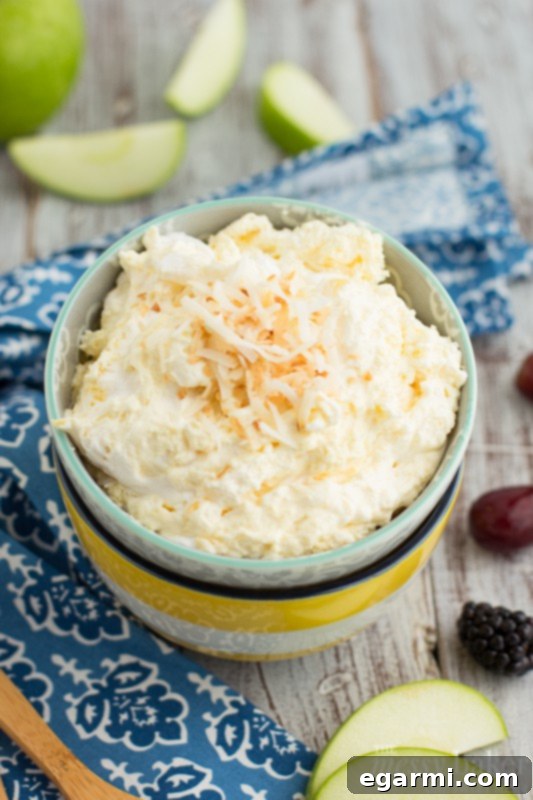 Close-up of a spoon scooping creamy Pina Colada Fruit Dip from a bowl, showing its smooth texture.