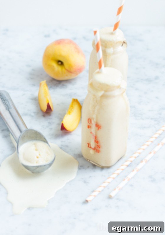 A hand holding a glass of Peach Pie Milkshake, illustrating its thick, creamy texture, perfect for a hot day.