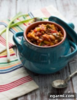 A close-up of a steaming bowl of Harvest Chili, garnished with cheese and scallions.