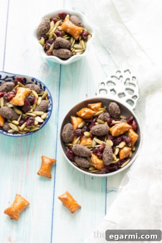 A mason jar filled with Easy Fall Trail Mix, brimming with roasted pumpkin seeds, dried cranberries, peanut butter filled pretzels, and dark chocolate covered almonds, ready to be enjoyed as a wholesome snack on a desk beside a computer, perfect for those working from home. www.themessybakerblog.com