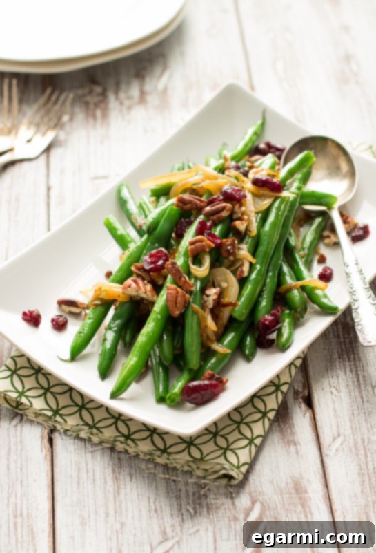 Close-up shot of an easy Thanksgiving side dish featuring bright green beans, glistening caramelized onions, and crunchy pecans, ready to be served.
