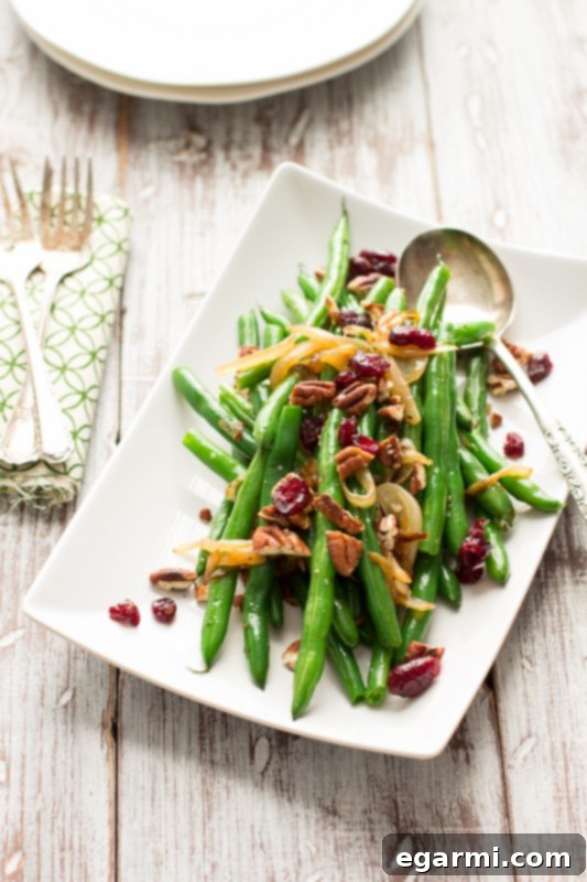 A close-up of the finished green bean side dish, garnished with pecans and cranberries, ready for a holiday meal.