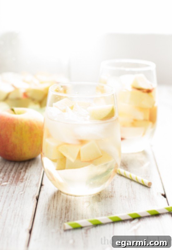 A glass of Sparkling Caramel Apple Sangria next to a pitcher