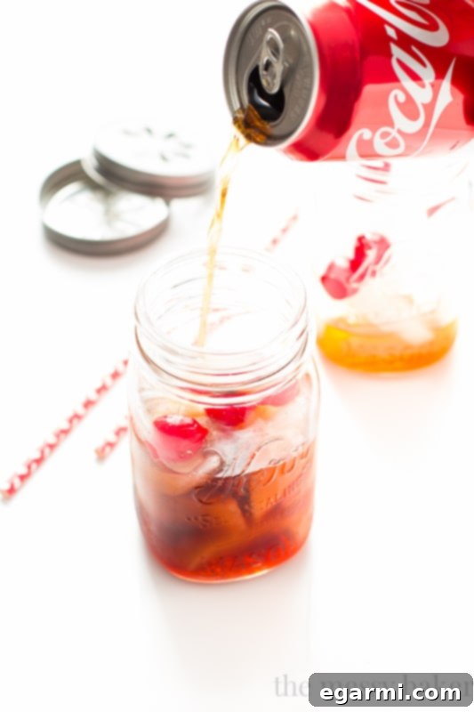 Ingredients for Black Cherry Cuba Libre laid out, including a can of cola, a bottle of black cherry rum, and maraschino cherries, emphasizing simplicity.