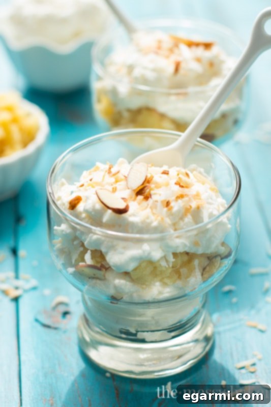 A glass serving of Pina Colada Fool, beautifully layered with cream, pineapple, and garnishes.