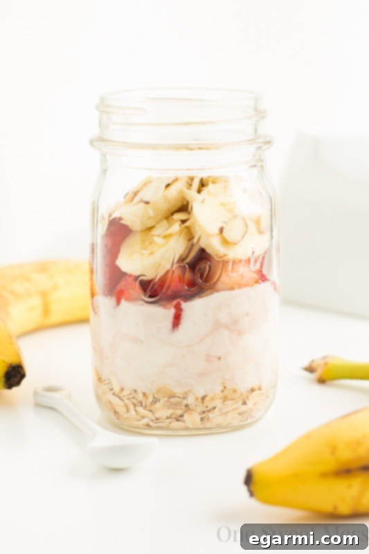 Preparing Strawberry Banana Overnight Oats: a person carefully folding sliced fruit into an oat mixture in a mason jar, illustrating the simple steps of meal preparation.