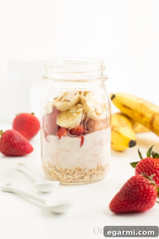 A close-up shot of Strawberry Banana Overnight Oats in a mason jar, revealing its creamy texture and vibrant fruit, with a spoon ready to scoop. Highlighting its delicious, dessert-like appeal.