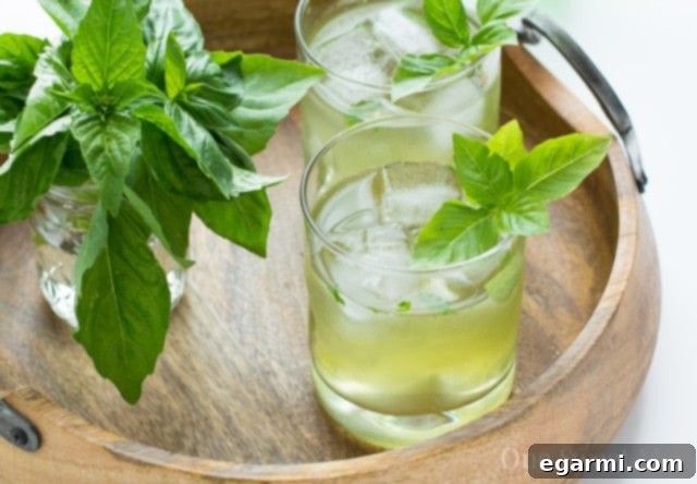 A hand muddling basil leaves and gin in a cocktail shaker