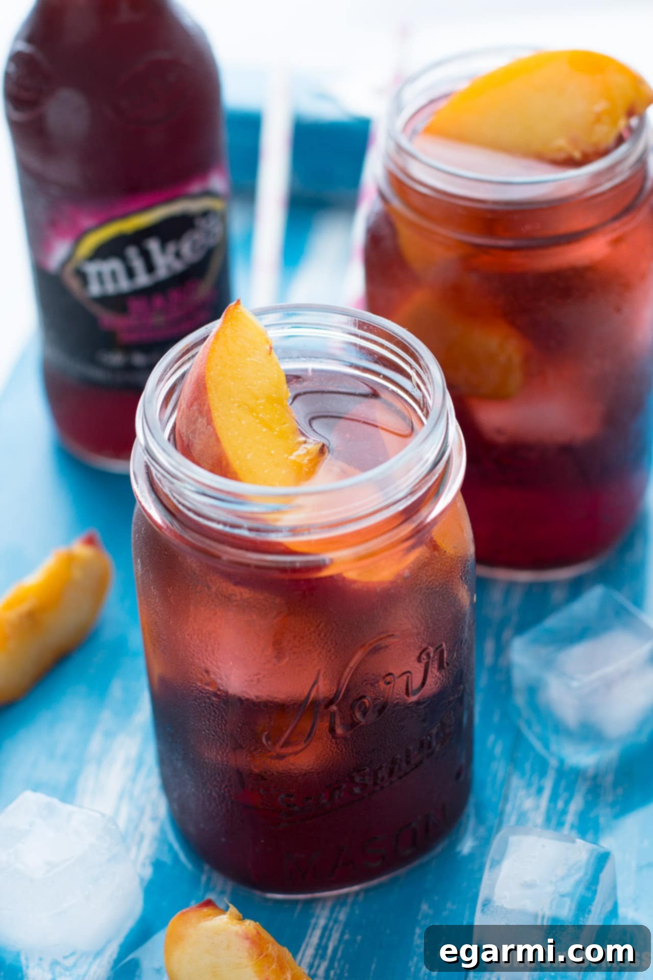 Two glasses of Black Cherry Peach Smash on a rustic outdoor table, set against a blurred background of a sunny backyard with trees.