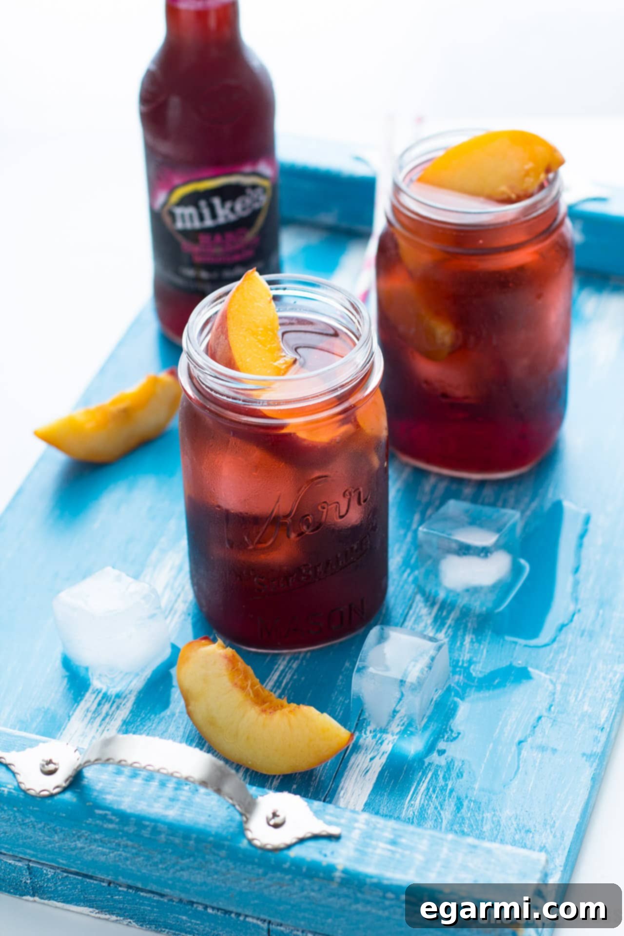 A Black Cherry Peach Smash cocktail being prepared outdoors, with fresh peaches and a bottle of Mike's Hard Black Cherry Lemonade visible.