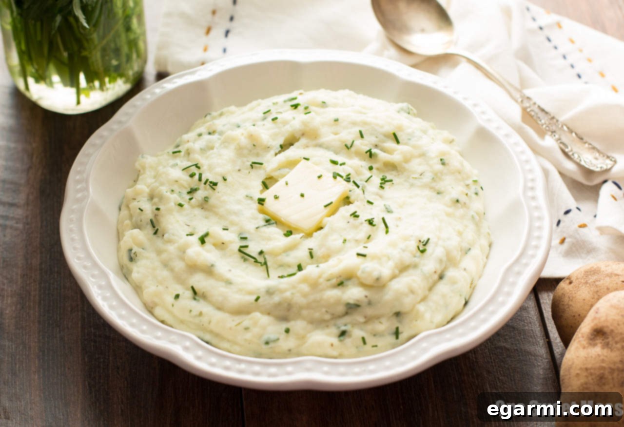 Fresh ingredients for mashed potatoes including Idaho potatoes, garlic, and herbs on a cutting board