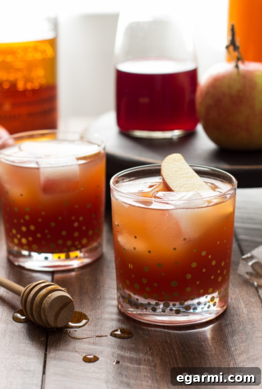 A bottle of honey next to a Pomegranate Cider Bourbon Splash cocktail