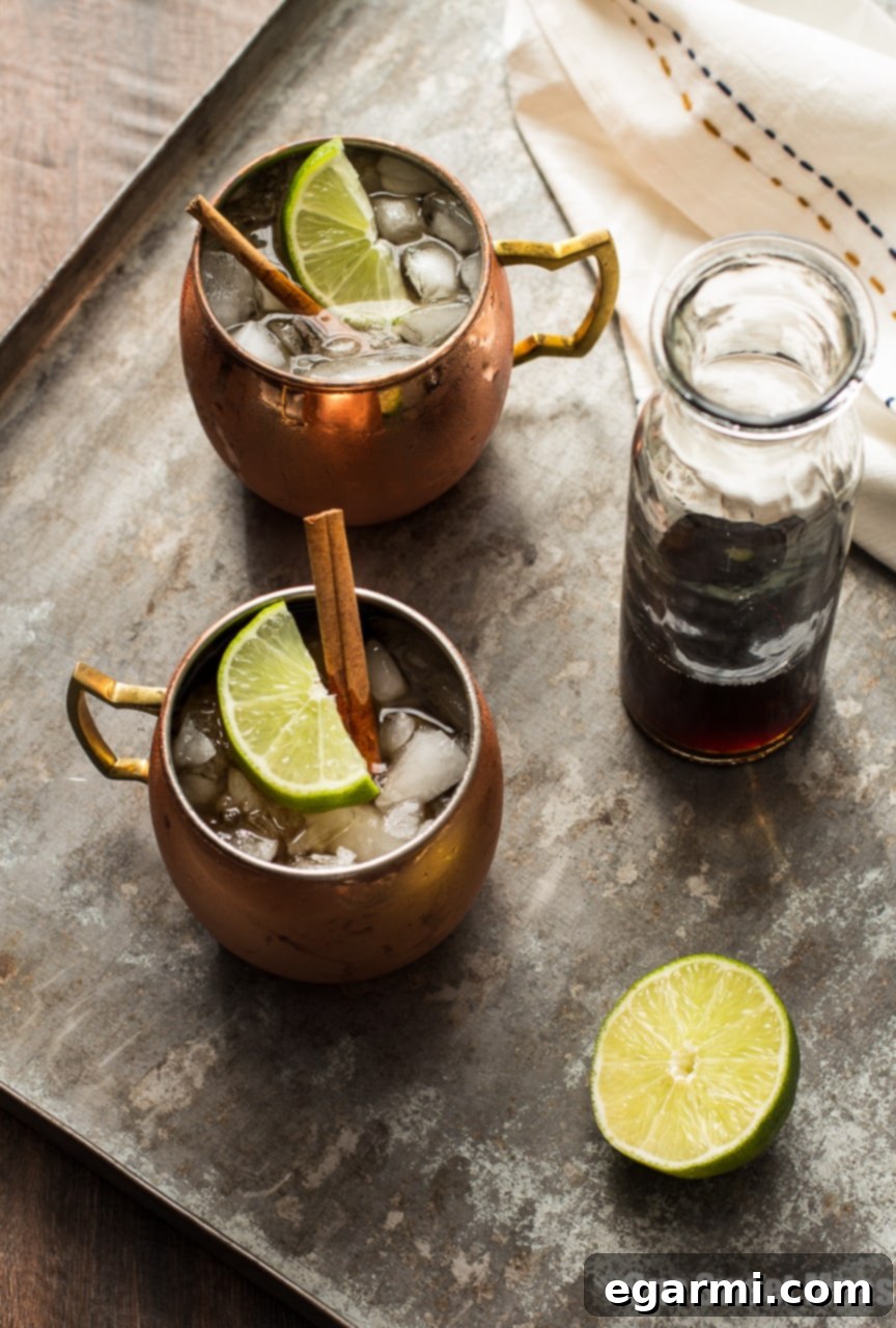 Close-up of a refreshing Mid-Winter Mule, highlighting the rich amber color of the bourbon and Pimm's blend, garnished with a lime wedge and cinnamon stick.