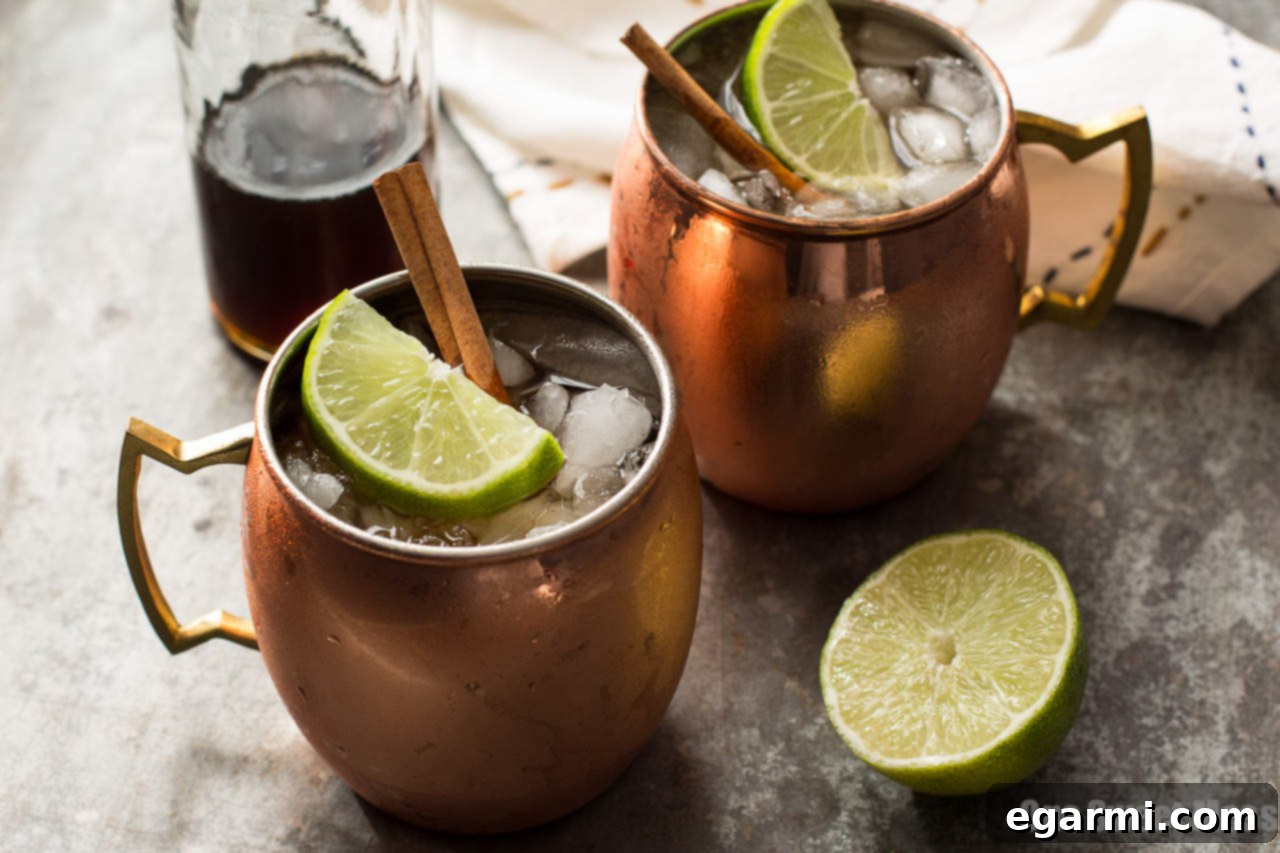 A chilled copper mug filled with the Mid-Winter Mule, showing crushed ice, a lime wedge, and a cinnamon stick, ready for a cozy evening.