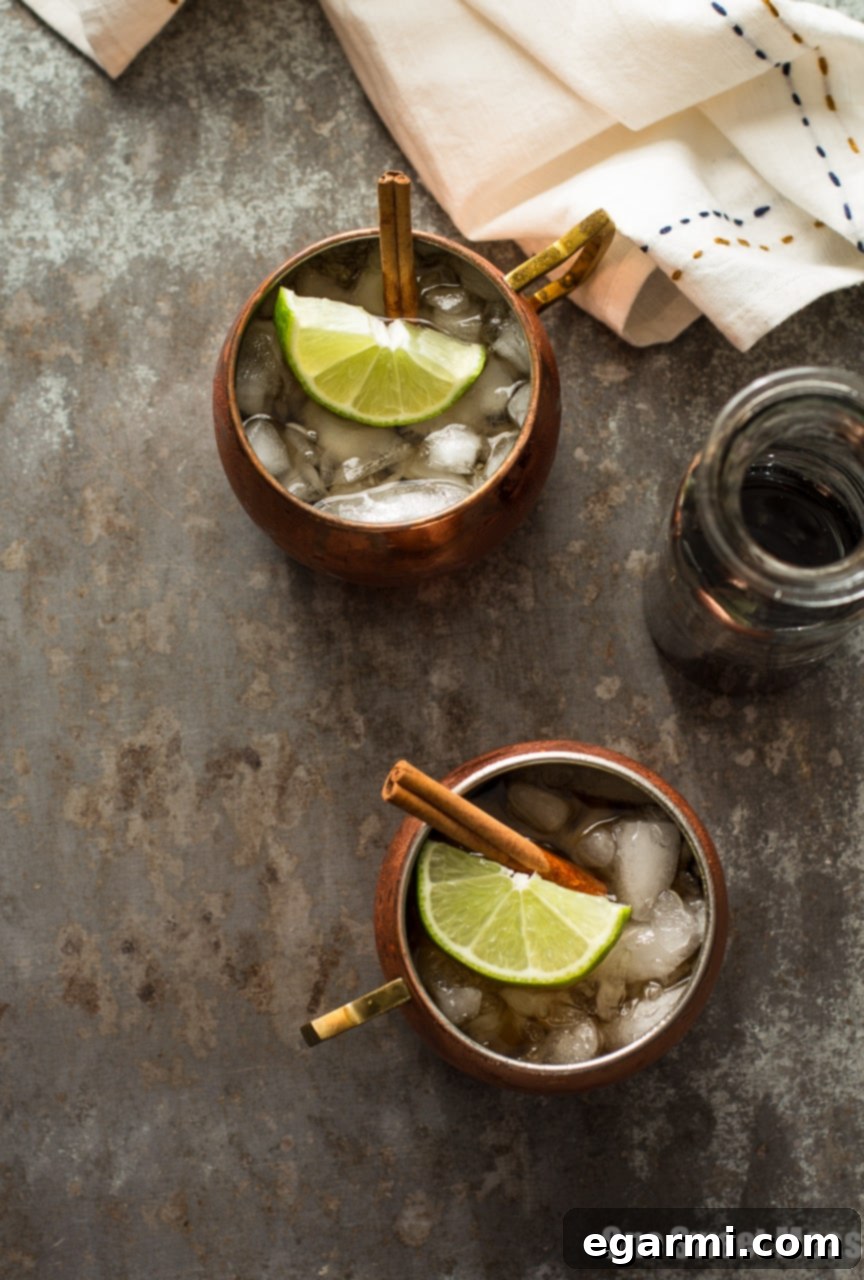 The Mid-Winter Mule cocktail on a rustic wooden surface, garnished with fresh lime and cinnamon, evoking a warm, inviting atmosphere.