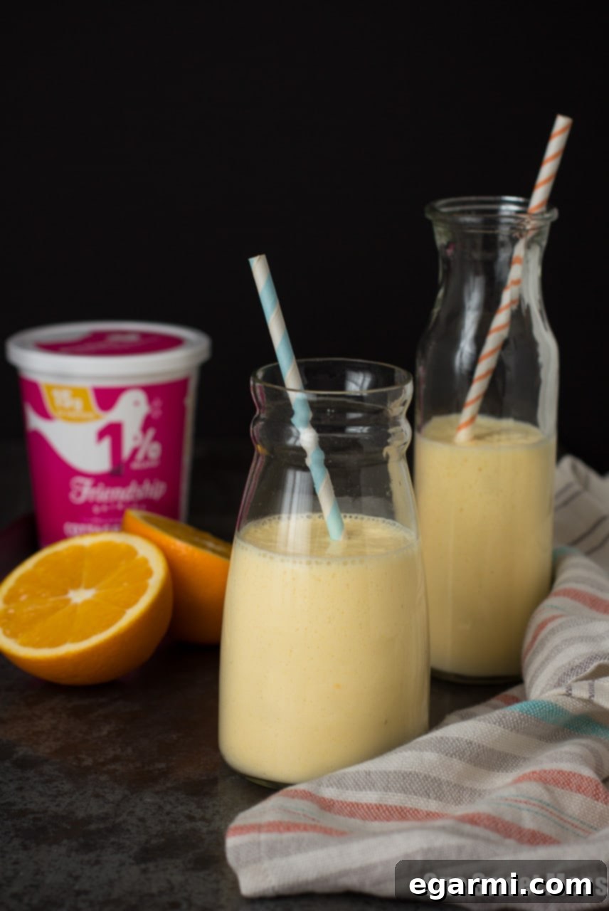 A tall glass of Dreamsicle Smoothie with a straw, garnished with fresh orange slices, showcasing its vibrant color and thick, inviting texture.